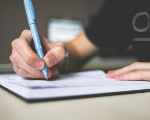 Close-up of hand writing in notebook using a blue pen, focus on creativity.